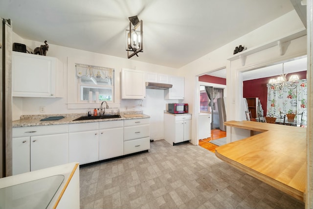 kitchen with white cabinetry, a notable chandelier, light floors, and a sink