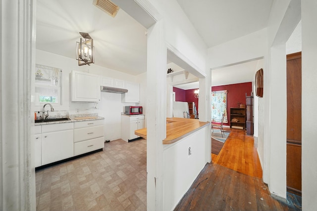 kitchen with under cabinet range hood, a chandelier, a sink, visible vents, and white cabinets