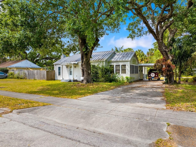 view of front of home with a front yard, a standing seam roof, concrete driveway, fence, and metal roof