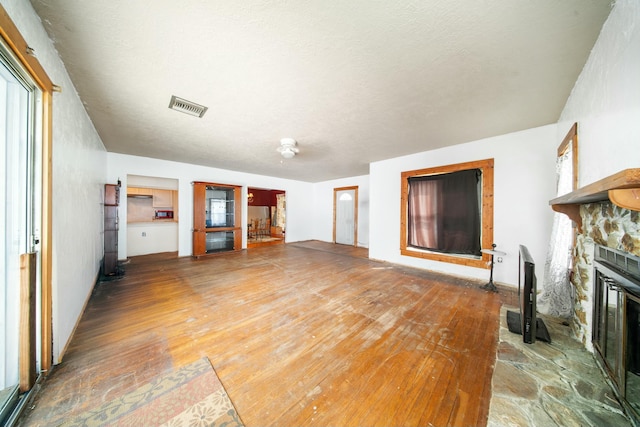 unfurnished living room featuring hardwood / wood-style floors, a stone fireplace, and visible vents