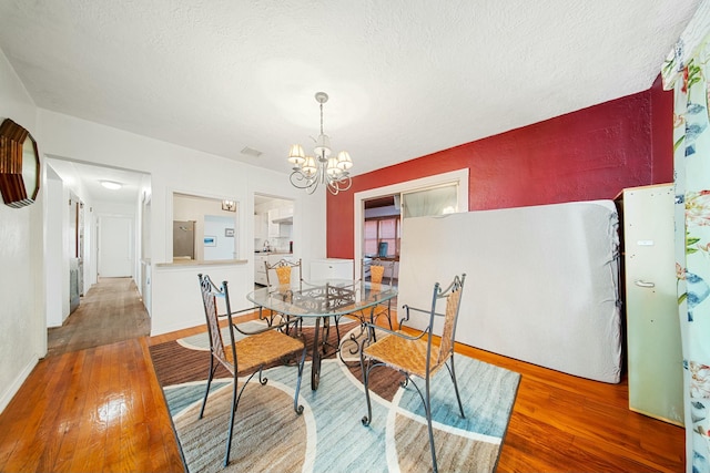 dining space with a textured ceiling, a notable chandelier, visible vents, and hardwood / wood-style floors