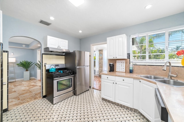 kitchen featuring visible vents, appliances with stainless steel finishes, arched walkways, under cabinet range hood, and a sink