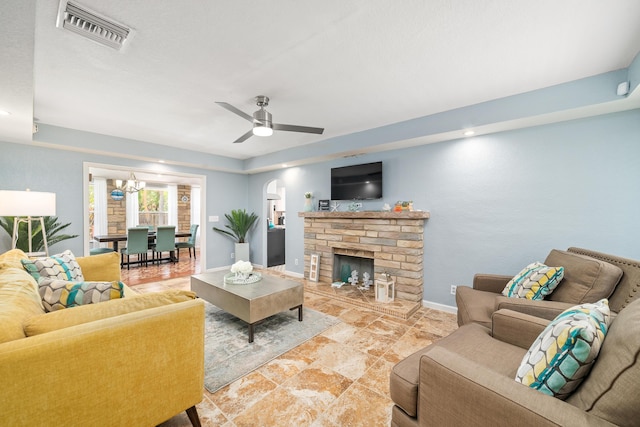 living area featuring visible vents, baseboards, a stone fireplace, arched walkways, and ceiling fan with notable chandelier