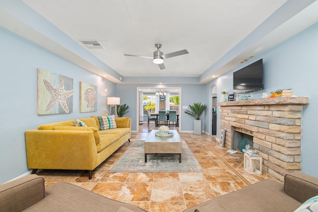 living area featuring a brick fireplace, baseboards, ceiling fan with notable chandelier, visible vents, and arched walkways