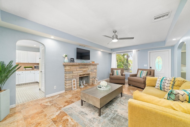 living room with baseboards, arched walkways, ceiling fan, visible vents, and a fireplace