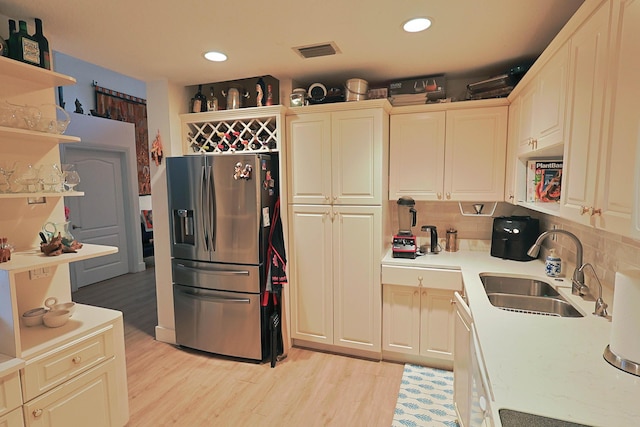 kitchen featuring visible vents, open shelves, stainless steel fridge, light countertops, and a sink