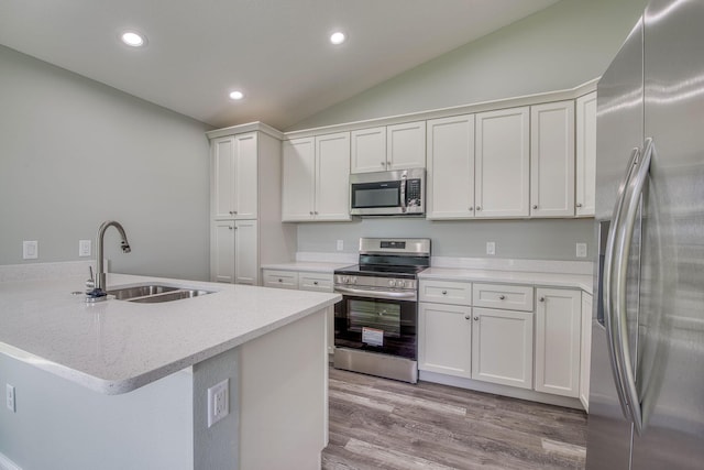 kitchen featuring stainless steel appliances, a peninsula, a sink, recessed lighting, and lofted ceiling