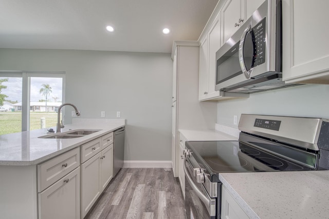 kitchen with white cabinets, a peninsula, a sink, light wood-style floors, and appliances with stainless steel finishes