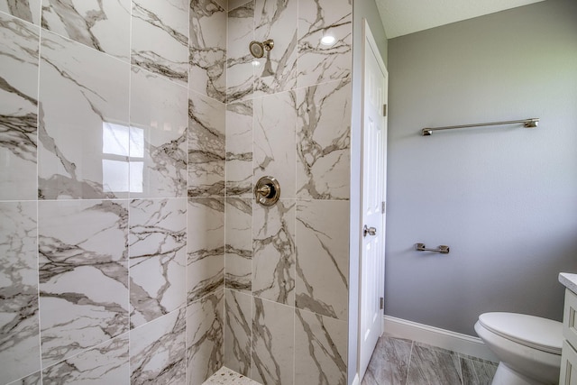 full bathroom featuring toilet, a tile shower, baseboards, marble finish floor, and vanity