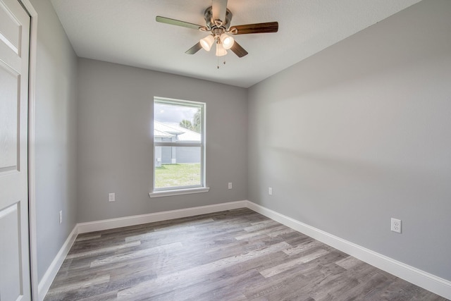 spare room with wood finished floors, a ceiling fan, and baseboards