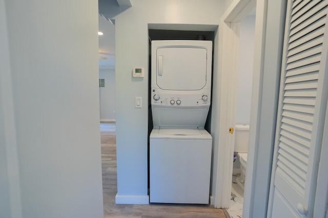 laundry area featuring stacked washer and clothes dryer, baseboards, laundry area, and light wood-type flooring