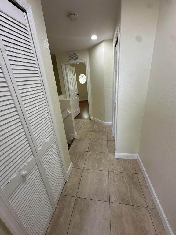 hallway featuring baseboards, visible vents, and light tile patterned floors
