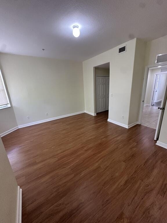 unfurnished room featuring baseboards, dark wood-style flooring, a textured ceiling, and visible vents