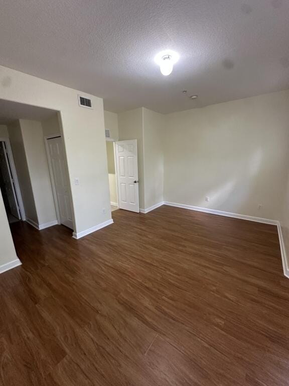 empty room with baseboards, a textured ceiling, visible vents, and dark wood finished floors