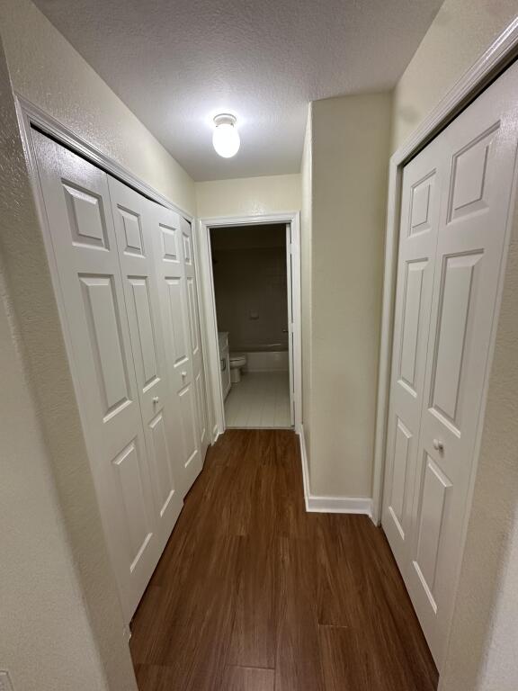 hall featuring a textured ceiling, baseboards, and dark wood finished floors