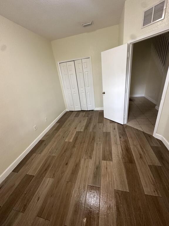 unfurnished bedroom with a closet, baseboards, dark wood-style floors, and visible vents