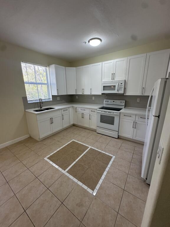 kitchen featuring white appliances, baseboards, white cabinetry, a sink, and light tile patterned floors