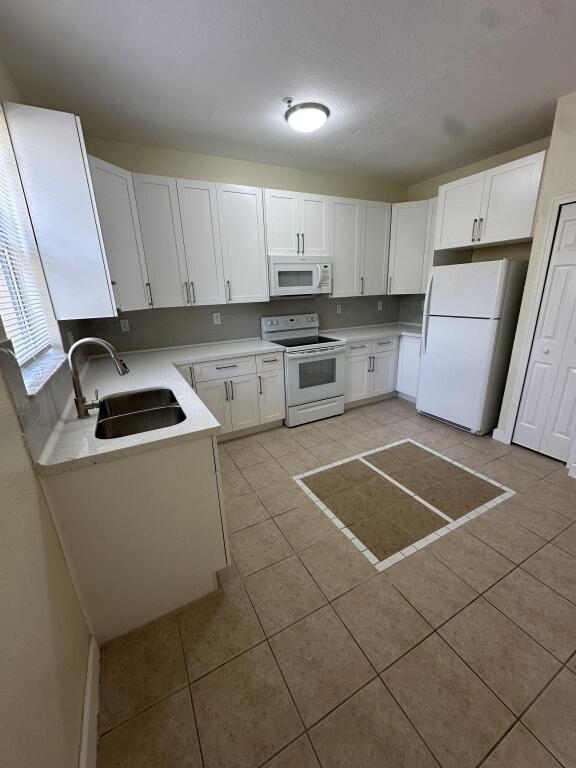 kitchen with light tile patterned flooring, light countertops, white appliances, white cabinetry, and a sink