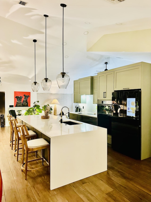 9494 Sun Pointe Dr, Boynton Beach, FL 33437 - kitchen with a sink, black refrigerator, wood finished floors, an island with sink, and vaulted ceiling