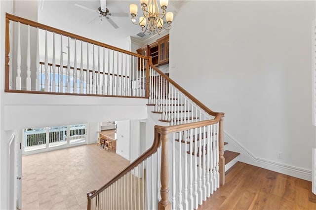 stairway with baseboards, a towering ceiling, ceiling fan with notable chandelier, and wood finished floors