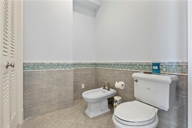 half bath with tile patterned floors, a wainscoted wall, toilet, and tile walls