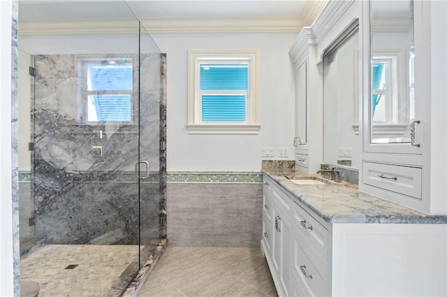 full bath featuring crown molding, wainscoting, vanity, a marble finish shower, and tile walls