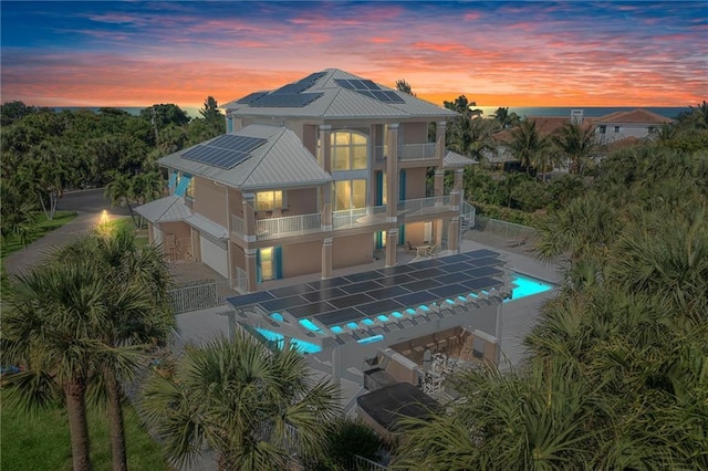 back of house at dusk featuring a fenced in pool, roof mounted solar panels, a balcony, a fenced backyard, and stucco siding