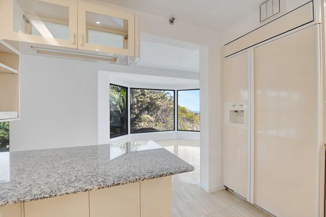 4605 S Ocean Blvd Unit 4C, Highland Beach, FL 33487 - kitchen with paneled refrigerator, light stone countertops, light tile patterned floors, glass insert cabinets, and cream cabinetry