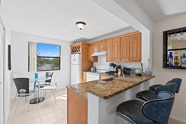 5661 Riverside Dr Unit 206B7, Coral Springs, FL 33067 - kitchen featuring white appliances, a sink, under cabinet range hood, baseboards, and a breakfast bar area