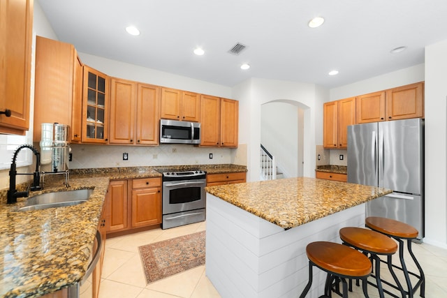 kitchen with stainless steel appliances, a kitchen island, a sink, stone countertops, and visible vents