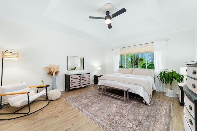 bedroom featuring ceiling fan, light wood-style floors, crown molding, and a raised ceiling