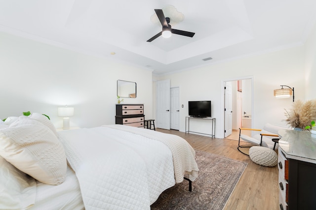 bedroom featuring a tray ceiling, crown molding, a ceiling fan, light wood-type flooring, and visible vents