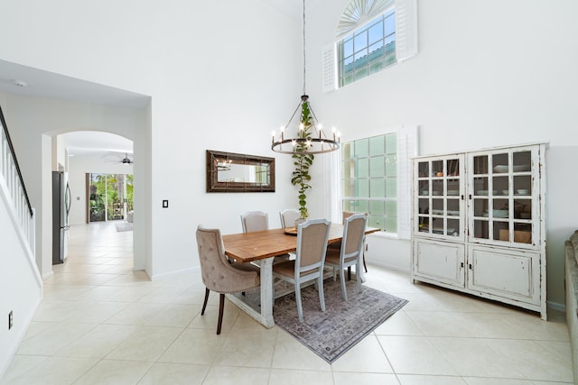 dining space with baseboards, a towering ceiling, arched walkways, ceiling fan with notable chandelier, and light tile patterned floors