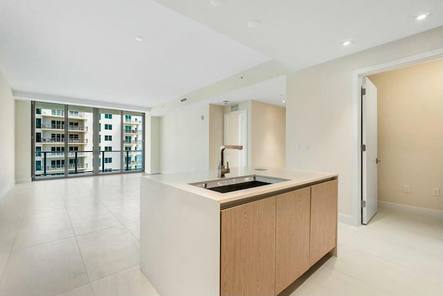 kitchen with open floor plan, baseboards, floor to ceiling windows, a center island with sink, and a sink