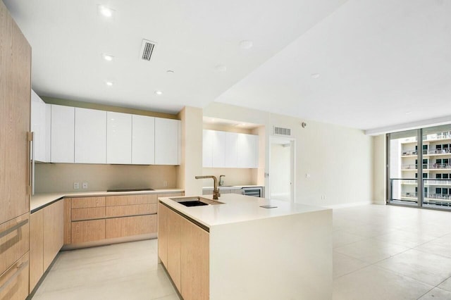 kitchen featuring visible vents, modern cabinets, a sink, and a kitchen island with sink