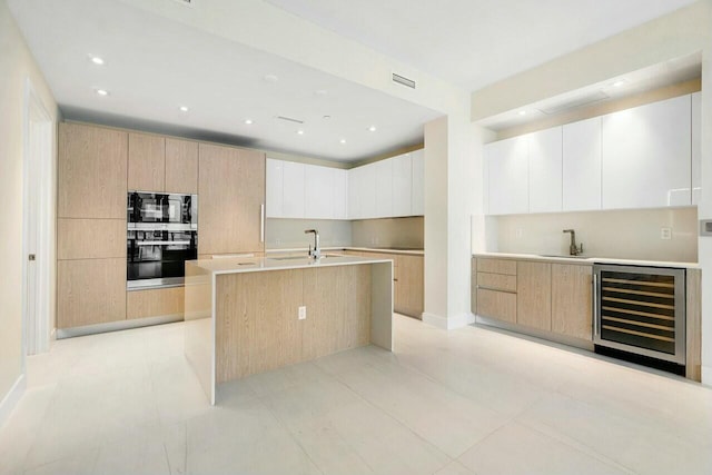 kitchen with a sink, modern cabinets, a center island with sink, beverage cooler, and visible vents