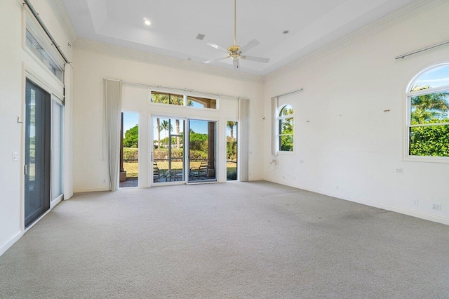 carpeted empty room featuring a towering ceiling, ornamental molding, a tray ceiling, and baseboards