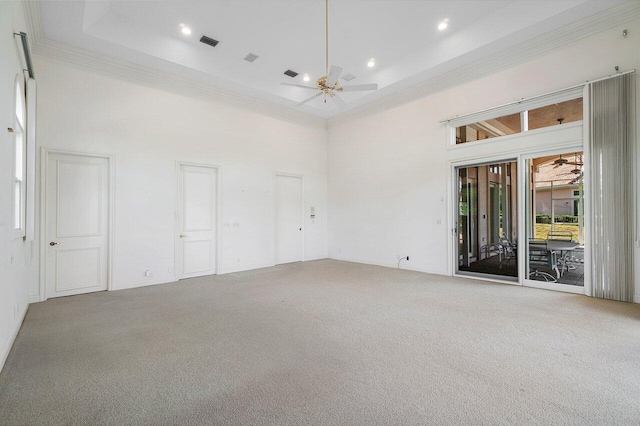 carpeted empty room featuring a ceiling fan, a towering ceiling, ornamental molding, and visible vents