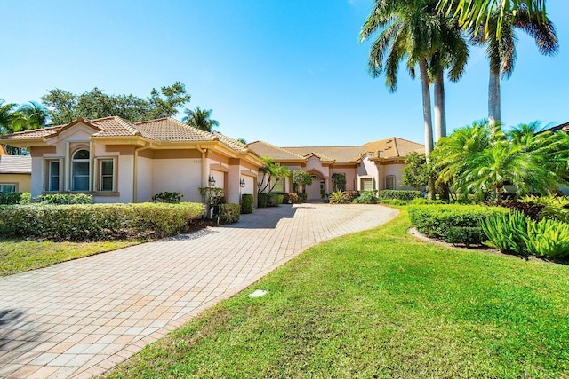mediterranean / spanish home with a front yard, stucco siding, a tiled roof, decorative driveway, and a garage