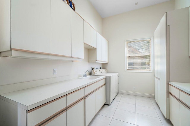 clothes washing area featuring washing machine and dryer, a sink, light tile patterned floors, baseboards, and cabinet space