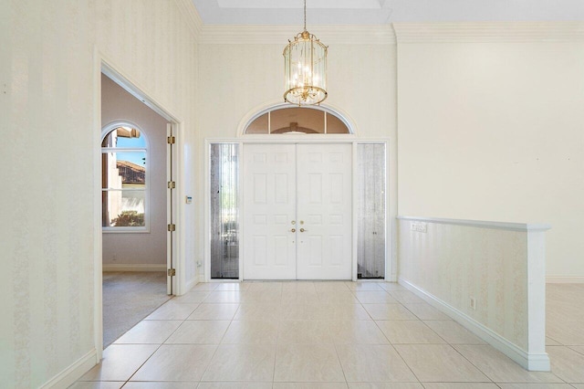 foyer entrance with an inviting chandelier, light tile patterned flooring, ornamental molding, and baseboards