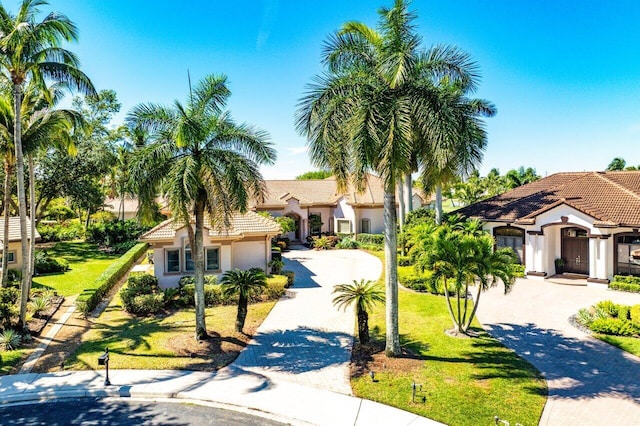 mediterranean / spanish-style home featuring a tile roof, decorative driveway, a front yard, and stucco siding