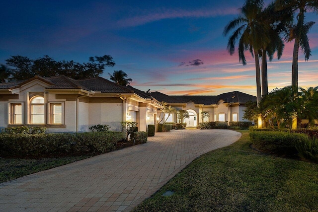 mediterranean / spanish house with stucco siding, an attached garage, a tiled roof, decorative driveway, and a front lawn