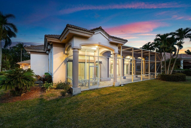 rear view of property with stucco siding, a tiled roof, a yard, and glass enclosure