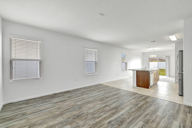 11265 SW Hadley St, Port Saint Lucie, FL 34987 - unfurnished living room with a textured ceiling, a sink, light wood-style floors, baseboards, and visible vents