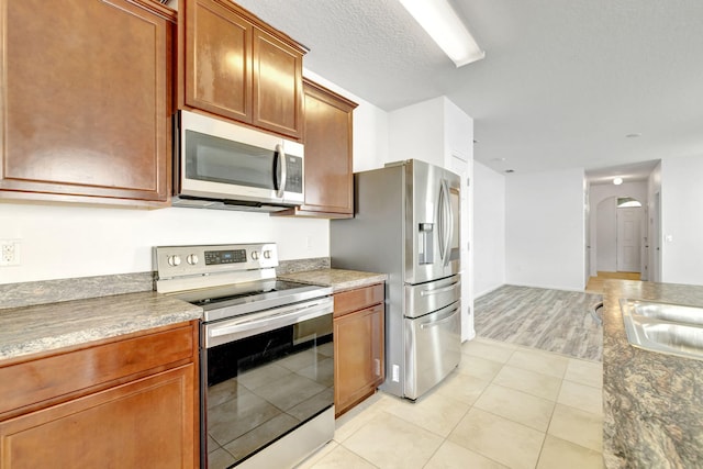 11265 SW Hadley St, Port Saint Lucie, FL 34987 - kitchen featuring a sink, arched walkways, light tile patterned floors, brown cabinetry, and appliances with stainless steel finishes