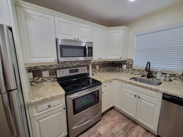 kitchen with wood finished floors, tasteful backsplash, appliances with stainless steel finishes, white cabinetry, and a sink