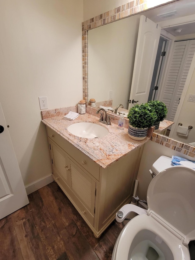 half bath with toilet, vanity, baseboards, and wood finished floors