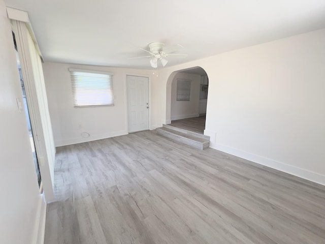 empty room with baseboards, wood finished floors, arched walkways, and a ceiling fan