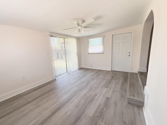 empty room featuring baseboards, wood finished floors, arched walkways, and ceiling fan